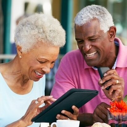 an old man looking besides an old woman smiling while holding a tablet